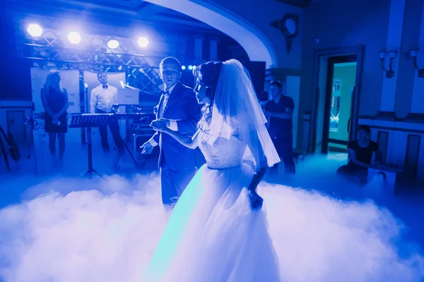 Wedding dance of newlywed couple. The hall is covered with white fume and filled by blue lights