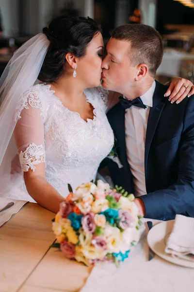 Happy newlyweds embracing and kissing in restaurant hall at the table