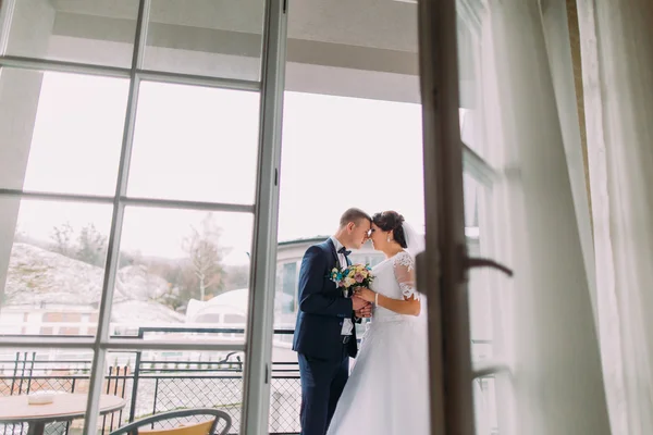 Enloved bride and elegant groom posing on balcony. Newlyweds honeymoon concept