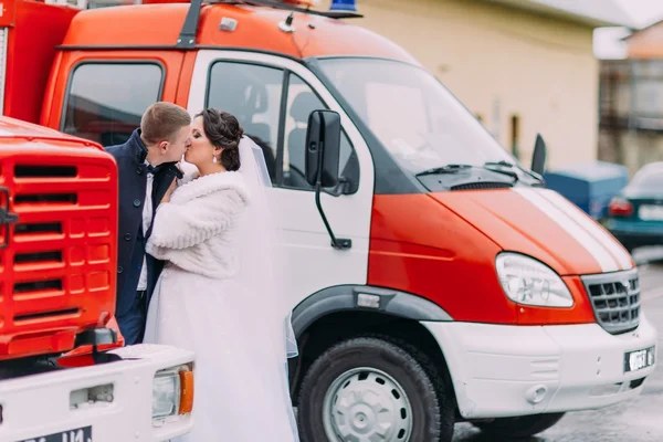 Happy wedding couple share kiss near red fire trucks