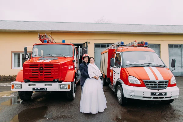 Happy wedding couple posing near two red fire trucks