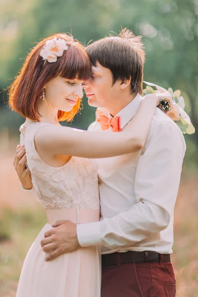 Handsome groom holds brides waist tenderly standing in the middle of forest meadow