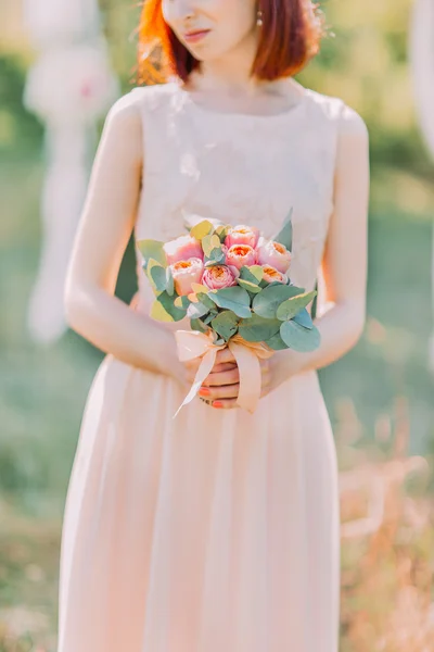 Charming caucasian woman wearing white wedding dress holding pink bouquet in her hands, close-up