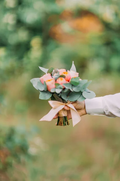 Wedding. Male hand holding a bouquet of pink flowers and greenery in green garden