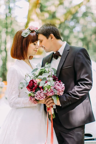 Handsome young groom and his beautiful redhair bride standing touching noses, enjoying marriage day