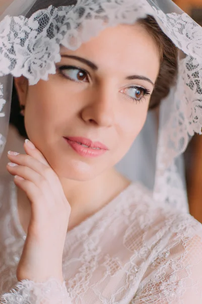 Close-up portrait of beautiful young and innocent bride in wedding dress with lifted veil posing indoors in dressing room