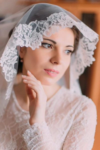 Close-up portrait of beautiful sensual bride in wedding gown with lifted veil posing indoors in dressing room