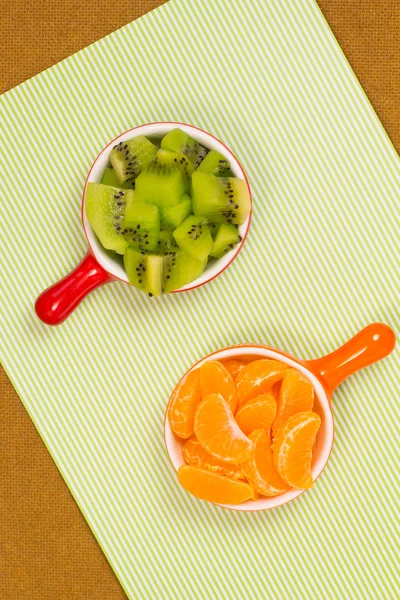 Slices of tangerine in  red cup. Slices of kiwi fruit in  orange cup