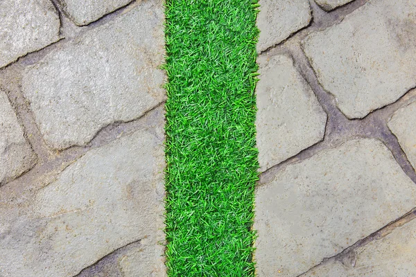 Line of plastic green grass on vertical center with gray brick f