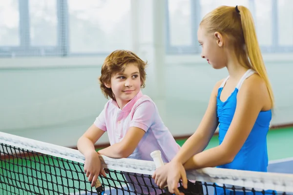 Cute children playing tennis and posing or resting in court indoor