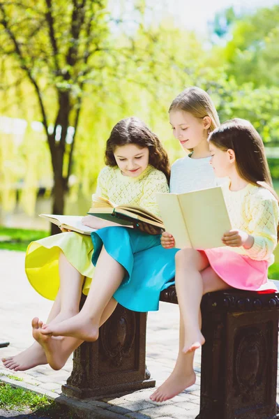 Children reading books at park. Girls sitting against trees and lake outdoor