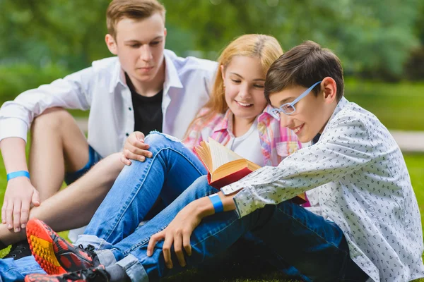 Smiling kids having fun and reading book at grass. Children playing outdoors in summer. teenagers communicate outdoor