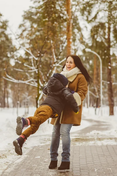 Happy family in winter clothing. laughing Mother and son playing fun game outdoor