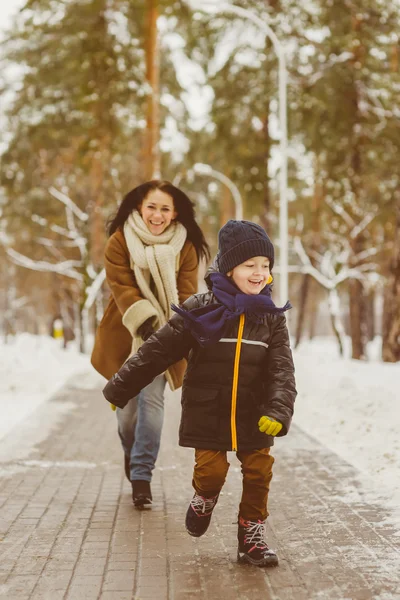 Happy family in winter clothing. Smiling son runs away from his mother outdoor