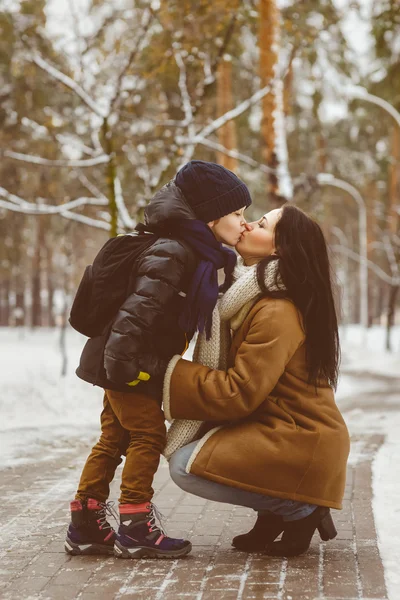 Happy family in winter clothing. Little son kissing his happy smiling mother