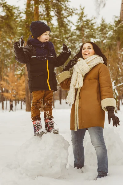 Happy family in winter clothing. laughing Mother and son playing fun game outdoor