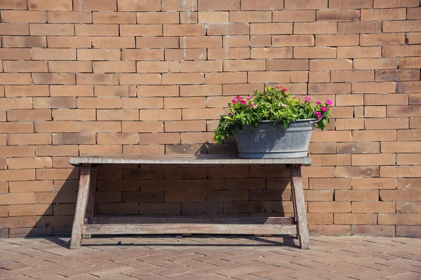 Flower bucket on a wood bench with red brick wall