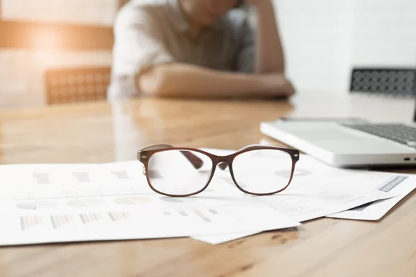 Woman with her hand holding his face taking a brake from working with laptop computer and static document with eye glasses on wooden desk. concept of stress resttension failed discourage