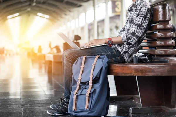 Man sitting with laptop. travel bag at the train station.vintage filter effected .