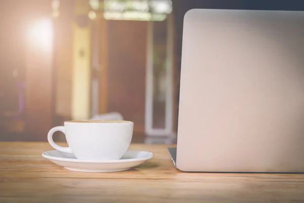 Coffee cup and laptop on wood table with vintage filter effect