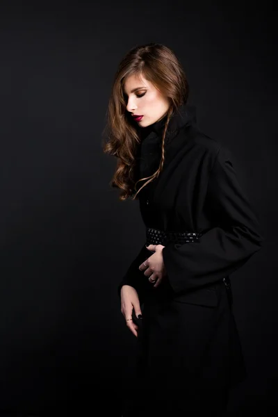 A brunette woman wearing a black coat with the laying and with red lips on a black background