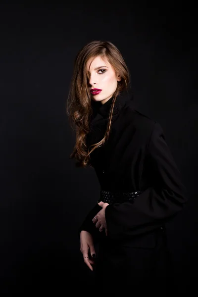 A brunette woman wearing a black coat with the laying and with red lips on a black background