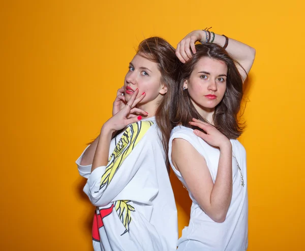 Close up fashion lifestyle portrait of two young hipster girls best friends, wearing bright make up and trendy clothes, making funny faces and have gray time. Urban  background.