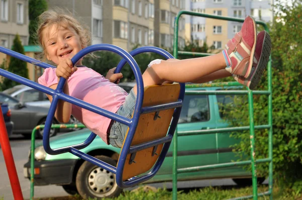 A little smiling girl enjoying swinging in a playground of an apartment house\'s court yard