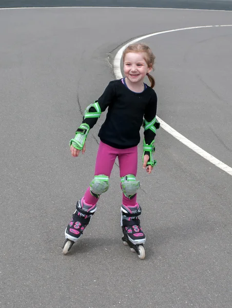 A little smiling girl practicing inline (roller) skating in the outdoor stadium