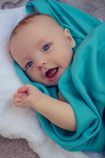 Smiling baby covered in blue blanket