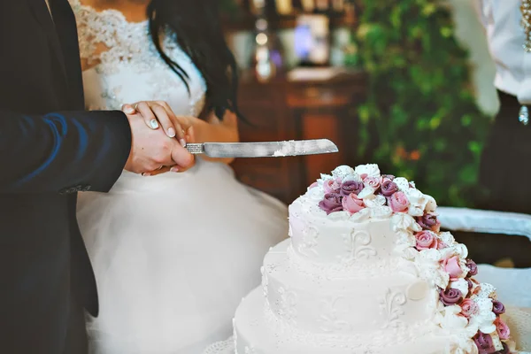 A bride and a groom is cutting their wedding cake with purple and white flowers