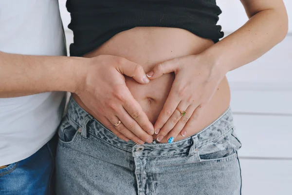 A young man and a beautiful young woman, look for tummy. In anticipation of the baby. Pregnant red-haired woman. holding hands on tummy in heart shape, happy anticipation of new life