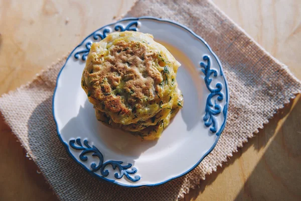 Vegetarian vegan diet snack, fritter on a plate of zucchini with herbs. Snack on a wooden surface.