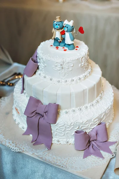Wedding cake in lilac purple color. With decorative bows, figurines blue bears on the cake.