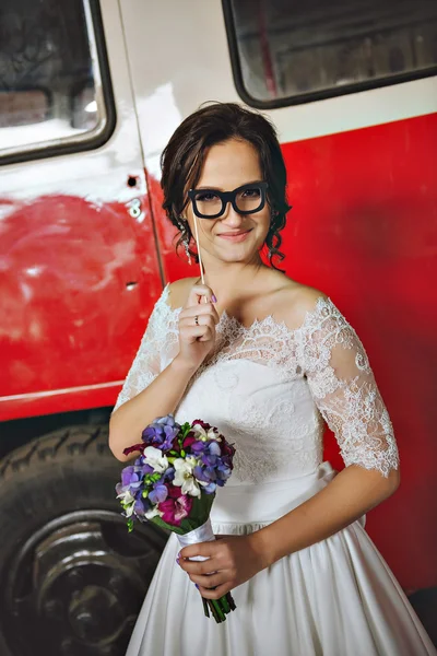 Beautiful happy bride in a red bus, with lilac lilac bouquet in her hands. In the hands of the decorative glasses on a stick.