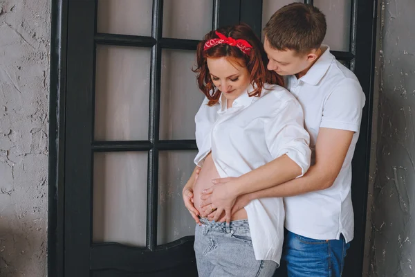 Joyful young man and a beautiful pregnant woman hugging each other. Laughing couple expecting a baby. Man embraces naked pregnant tummy. We look at each other and hug the midsection.