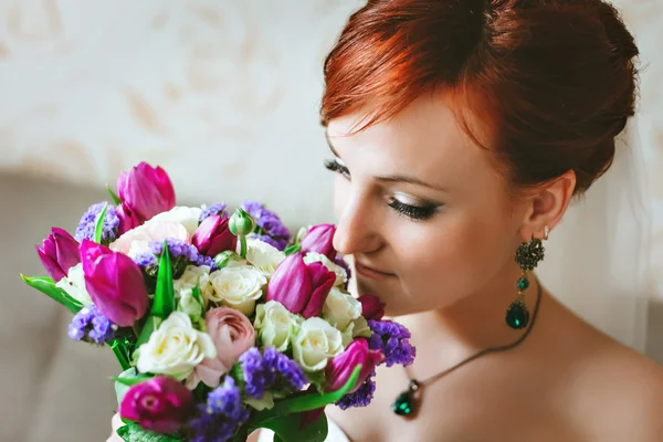 Young beautiful Bride holding a bouquet of purple pink. Red hair. Looking at flowers