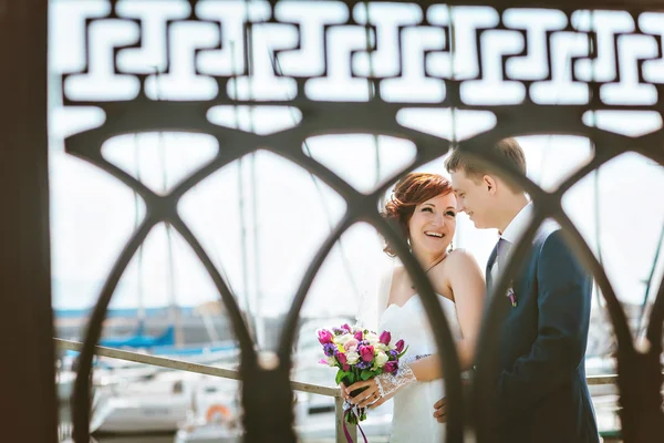Smiling happy couple on bridge wedding day, bride white dress with train, groom in blue suit.