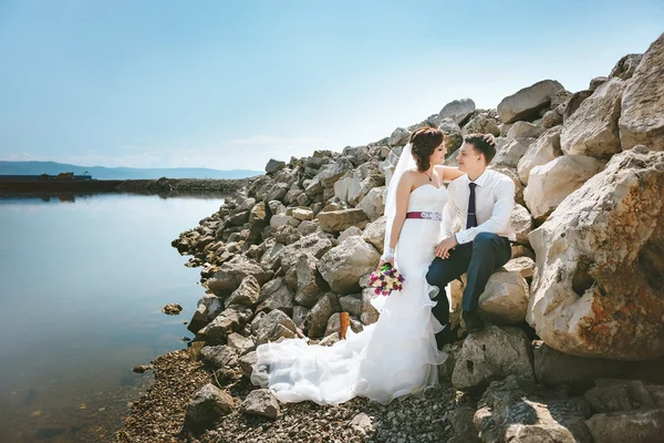 Happy smiling young bride and groom, walking on beach, kissing, hugging wedding ceremony near rocks, ocean.