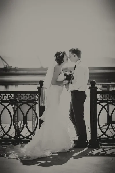 Smiling happy couple on bridge wedding day, bride white dress with train, groom in blue suit.