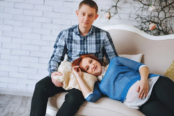 Pregnant young couple in love couch. woman lay on knees of men. husband embraces his wife. With colors rose quartz and sky blue.