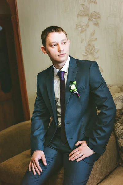 Portrait  young groom in a blue suit sitting on the couch