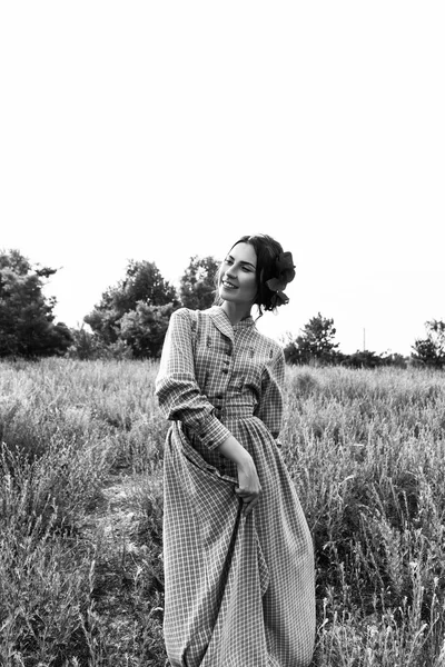 Outdoor portrait of a beautiful brunette woman in dress with flowers in her hair in the field. Black and white photo