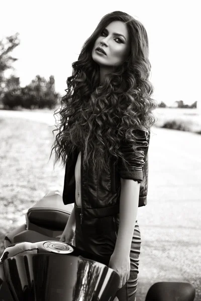 Sexual biker woman wearing black leather jacket with her sport motorcycle on a highway. Beauty, fashion. Adventure and freedom. Black and white photo