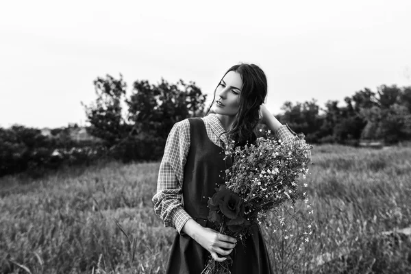 Outdoor portrait of a beautiful brunette woman in blue dress in the field. Black and white photo