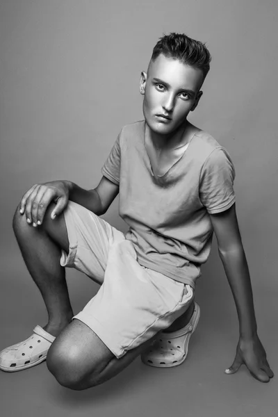 Vertical portrait of young man in casual clothes sitting in studio. Black and white