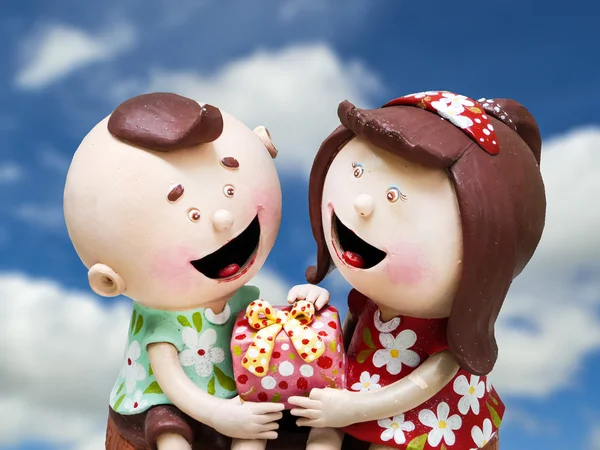 Ceramic doll boy and girl and gift on hands blue sky