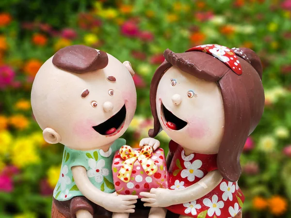 Ceramic doll boy and girl and gift on hands  flower garden backg