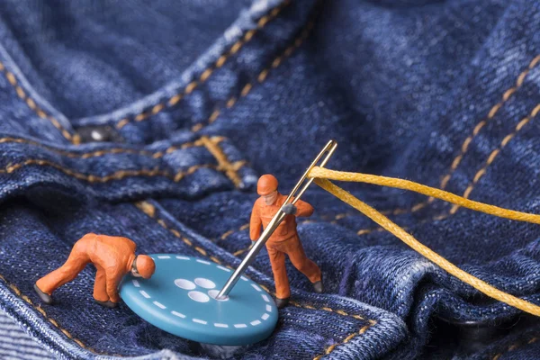 The concept for the fashion industry. Miniature workers sew on b