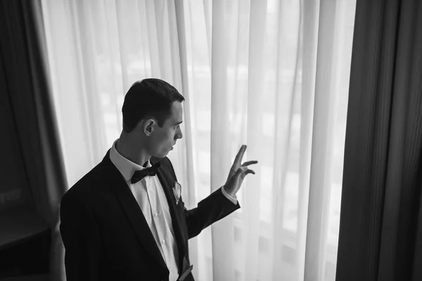 A man in a tuxedo looking out the window.
